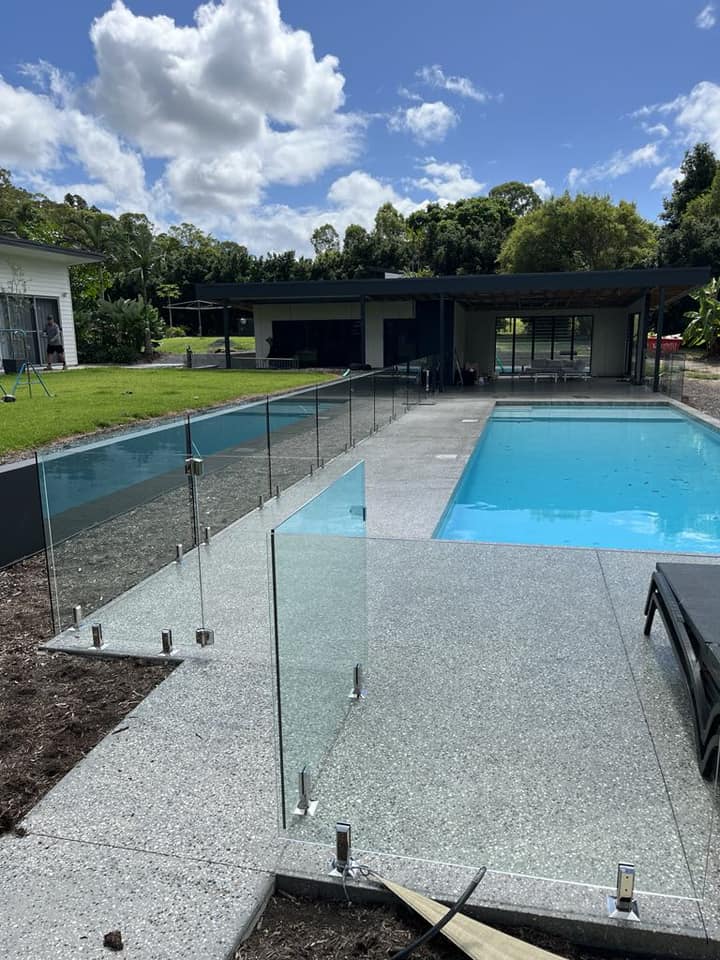 Frameless glass pool fence with polished stainless spigots on exposed aggregate